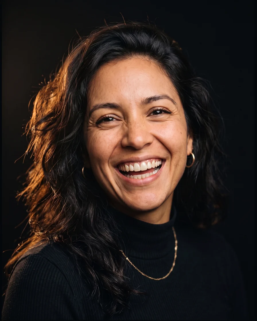 Decorative model laughing with a bright, harmonious ceramic smile design, editorial portrait on a black background with warm light. Not a patient.
